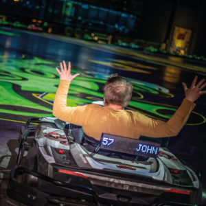 Un joueur BattleVirus dans son kart lève les bras parce que touché par le virus vert devant lui